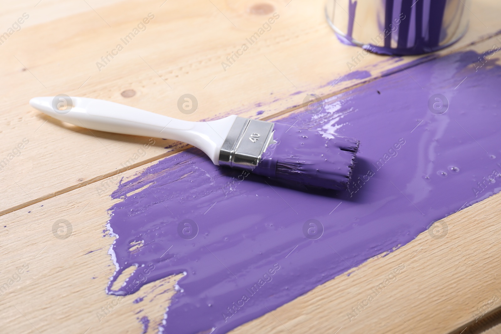 Photo of Smear of violet paint, can and brush on wooden table, closeup