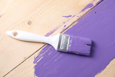 Photo of Smear of violet paint and brush on wooden table, top view