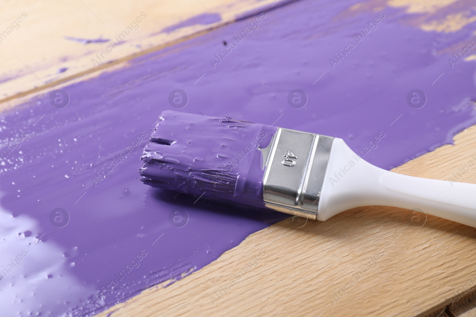 Photo of Smear of violet paint and brush on wooden table, closeup