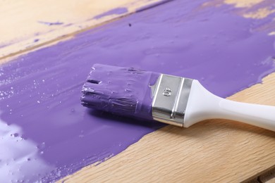 Photo of Smear of violet paint and brush on wooden table, closeup