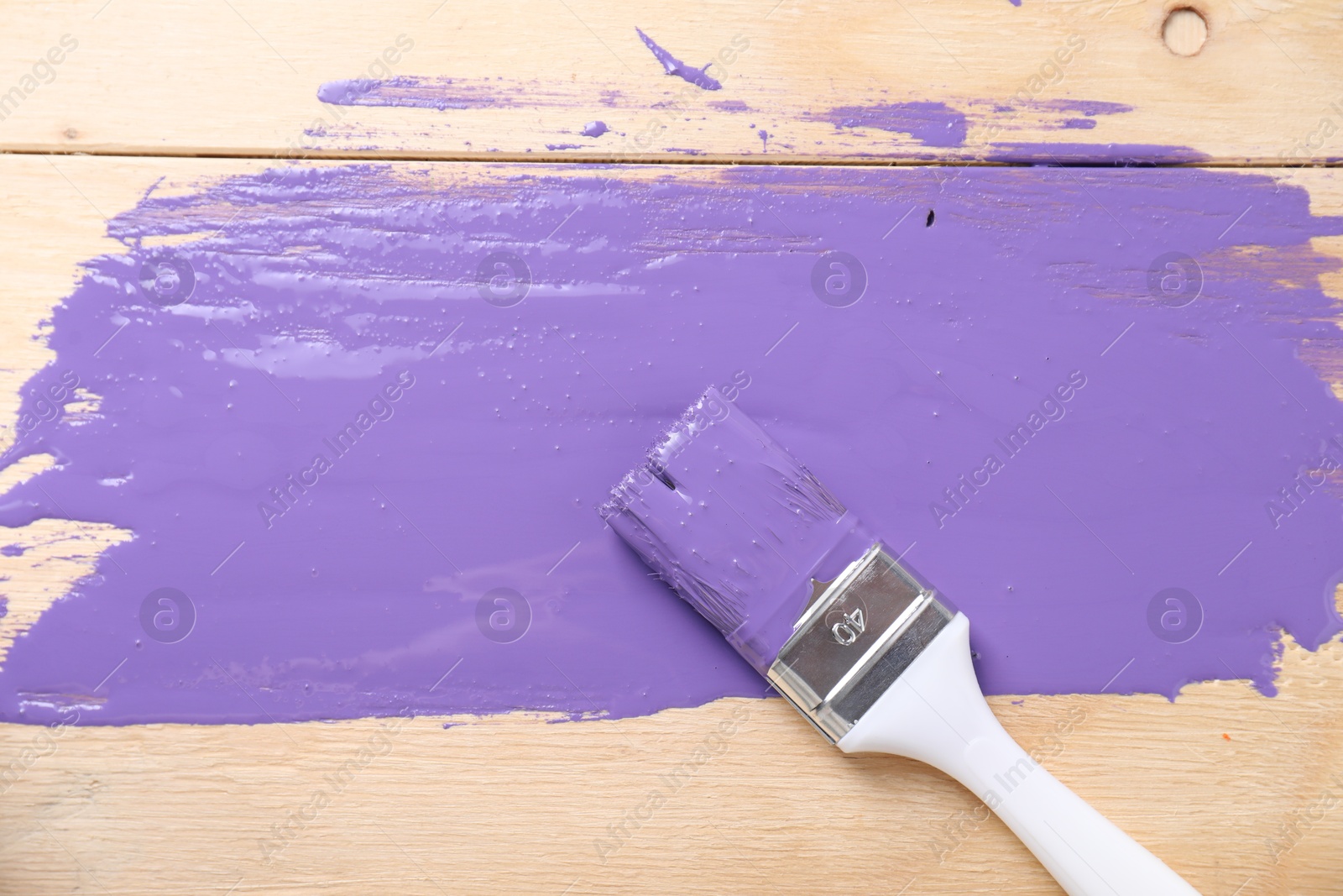 Photo of Smear of violet paint and brush on wooden table, top view