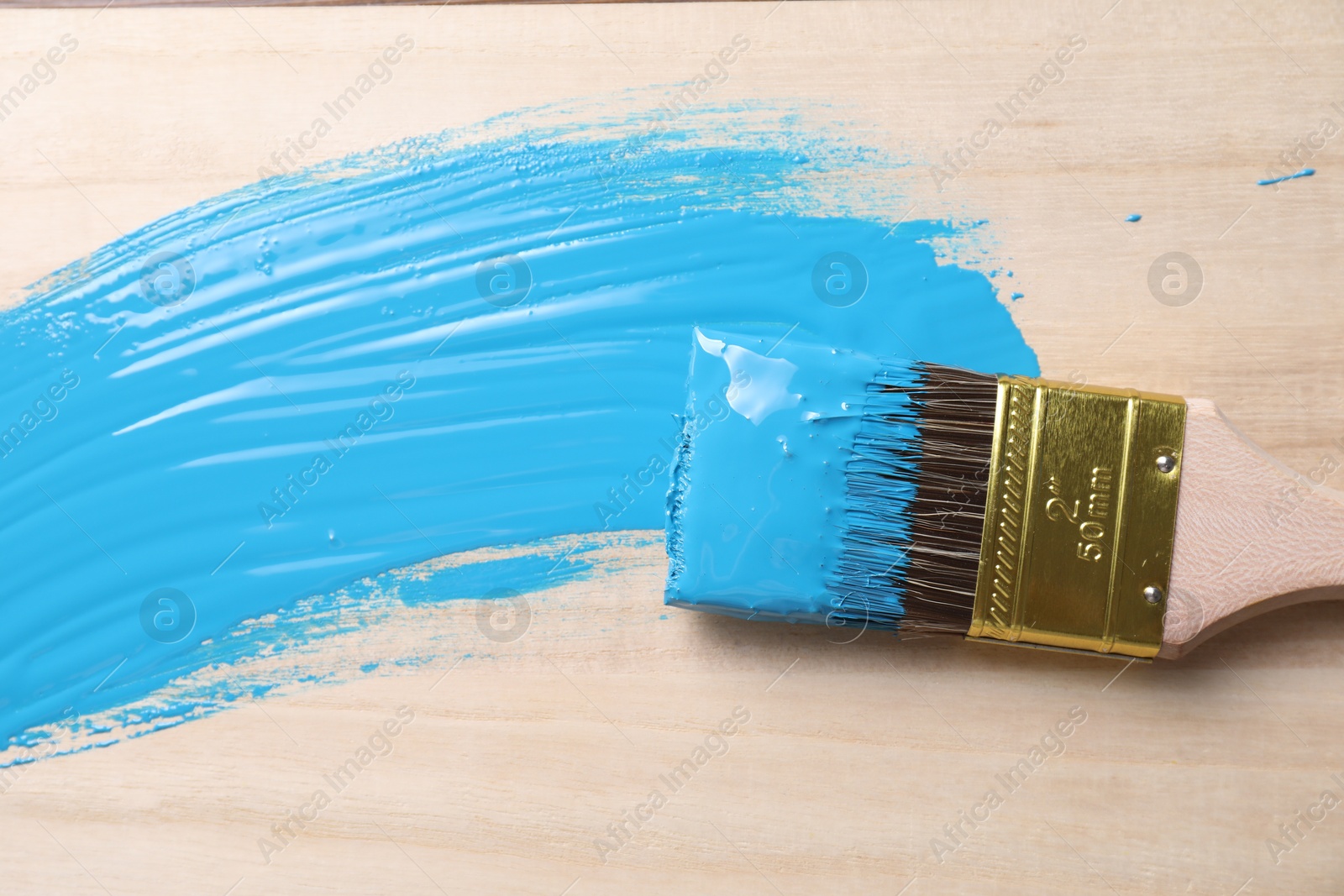 Photo of Smear of light blue paint and brush on wooden table, top view