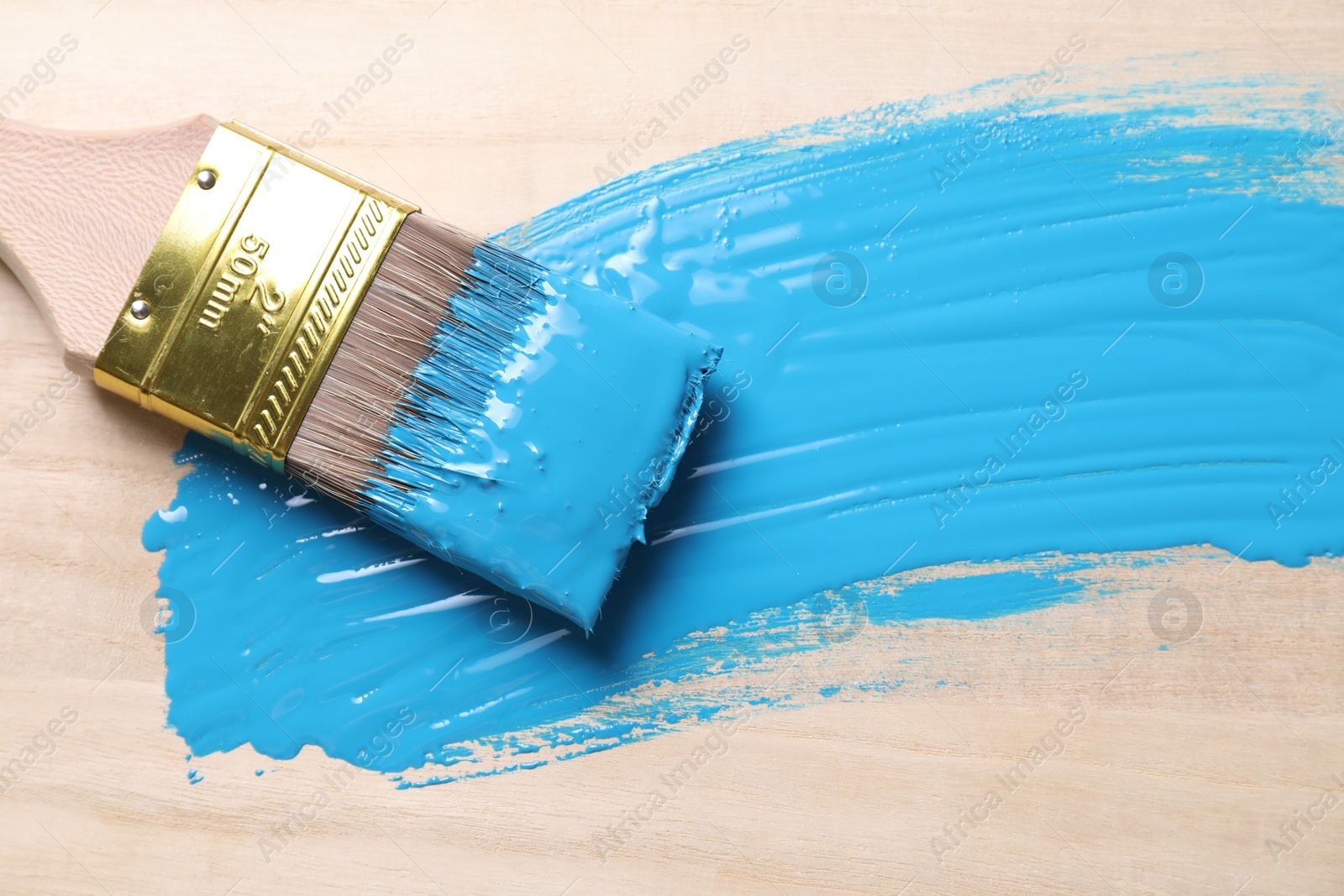 Photo of Smear of light blue paint and brush on wooden table, top view