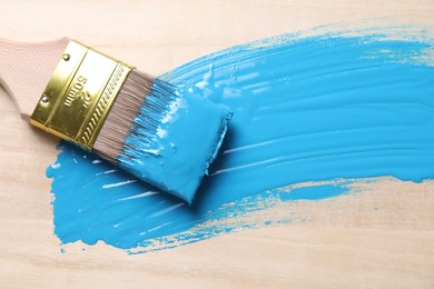 Photo of Smear of light blue paint and brush on wooden table, top view