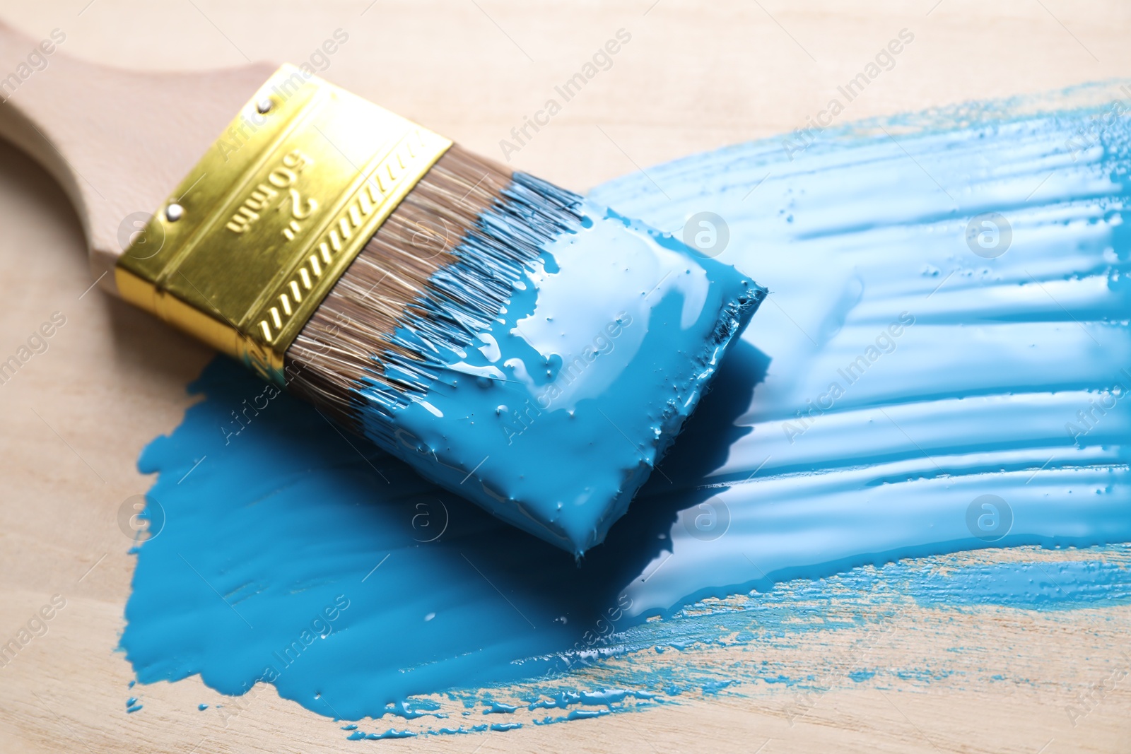 Photo of Smear of light blue paint and brush on wooden table, closeup