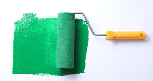 Photo of Smear of green paint and roller on white background, top view