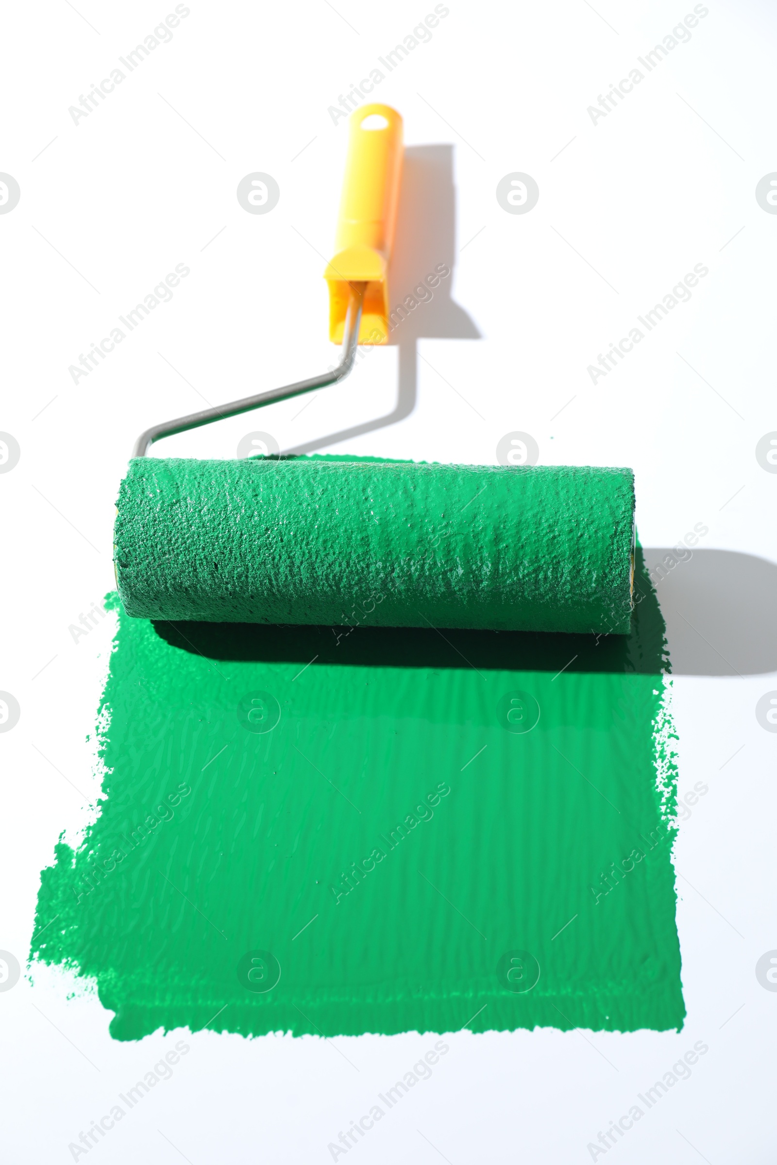 Photo of Smear of green paint and roller on white background, closeup