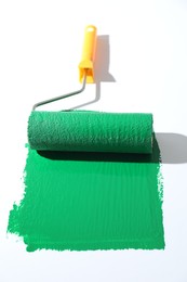 Photo of Smear of green paint and roller on white background, closeup