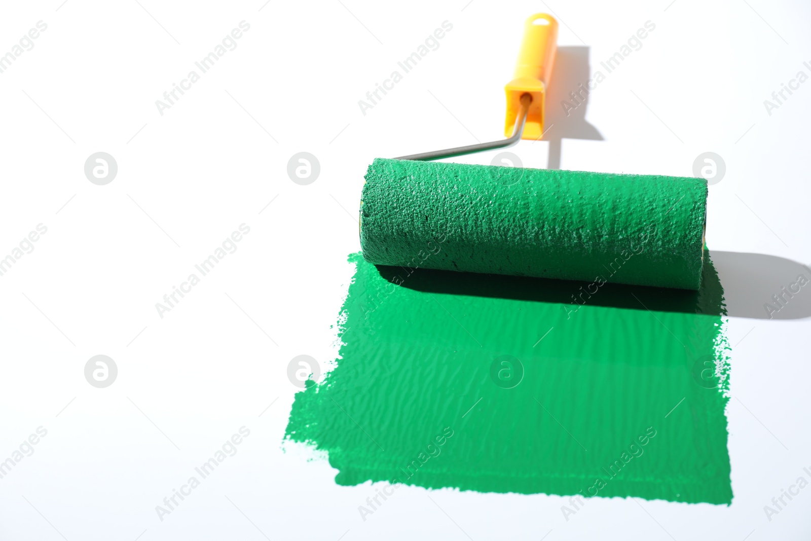 Photo of Smear of green paint and roller on white background, closeup. Space for text