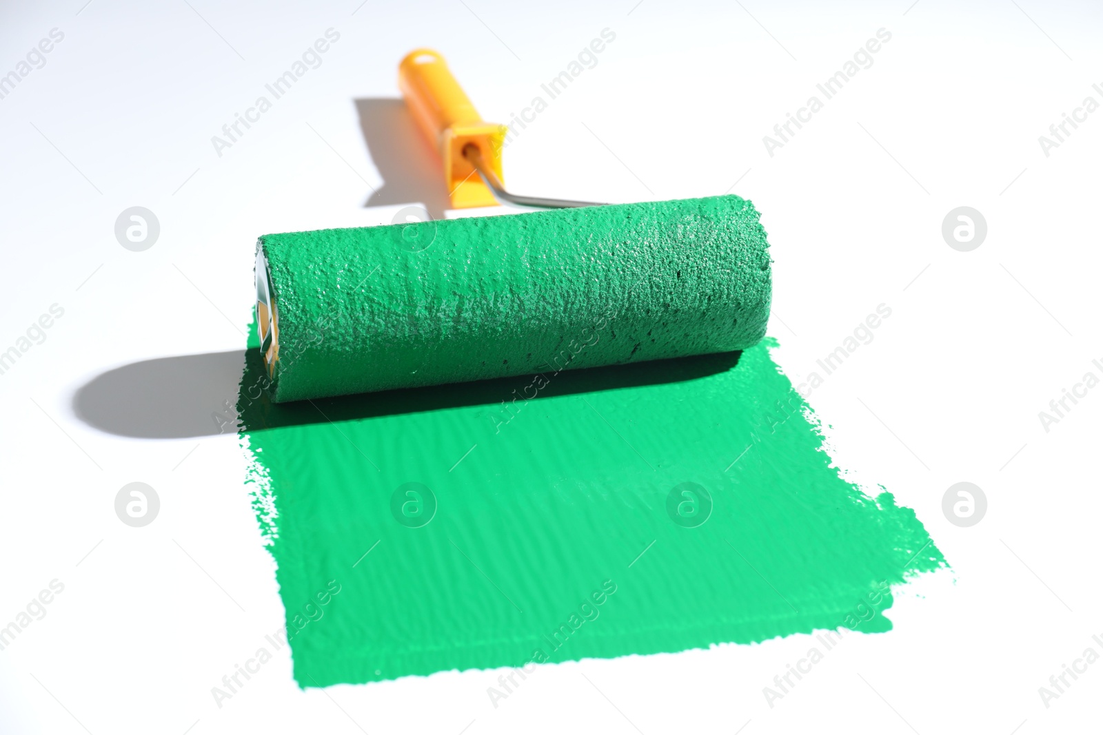 Photo of Smear of green paint and roller on white background, closeup