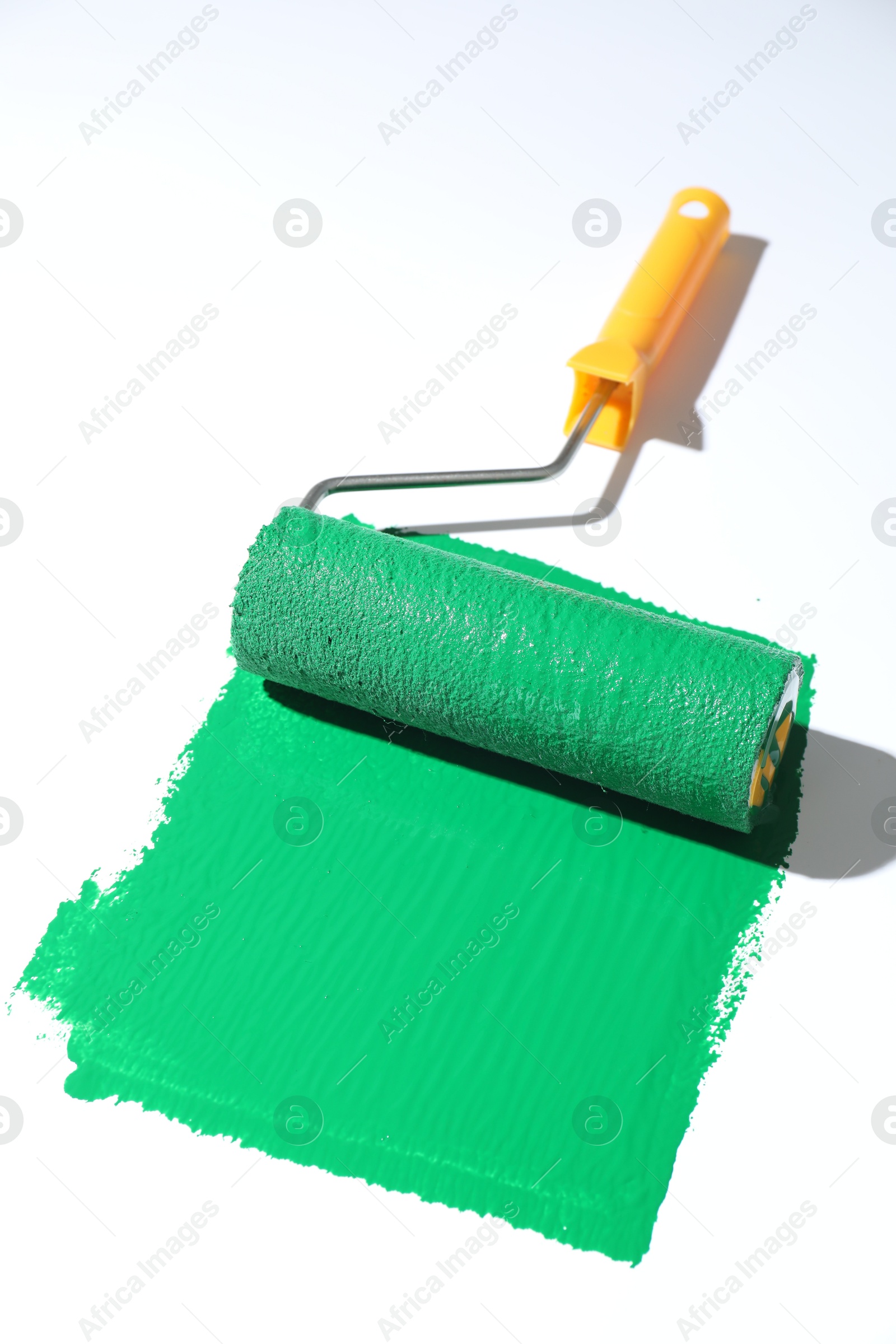 Photo of Smear of green paint and roller on white background, closeup