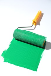 Photo of Smear of green paint and roller on white background, closeup