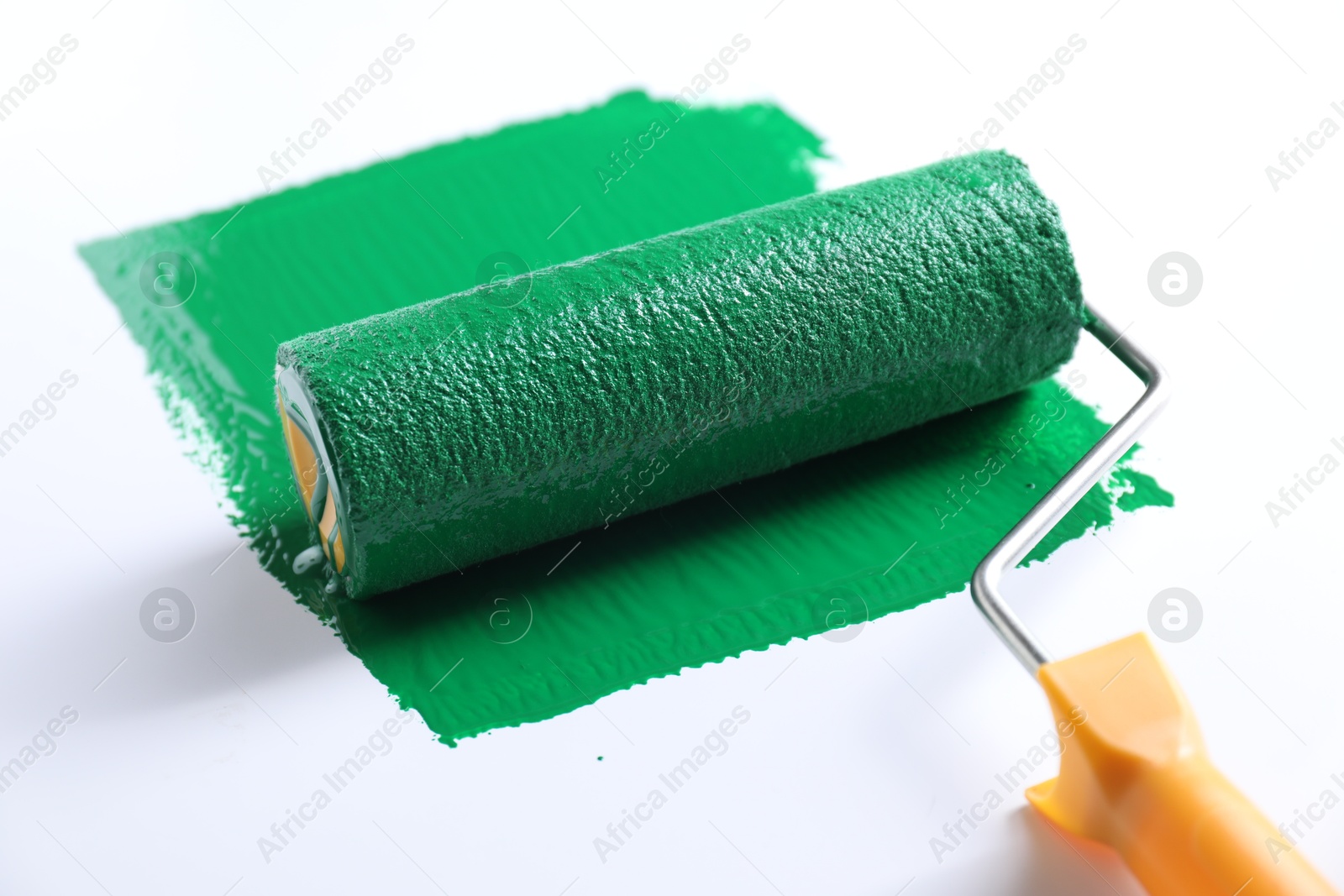 Photo of Smear of green paint and roller on white background, closeup