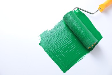 Photo of Smear of green paint and roller on white background, top view. Space for text