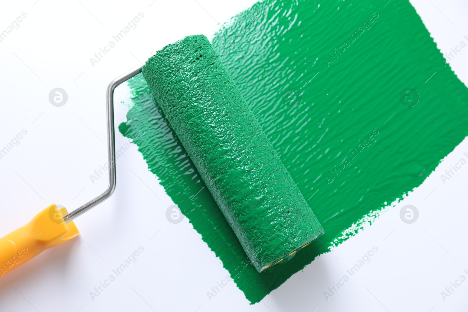 Photo of Smear of green paint and roller on white background, top view