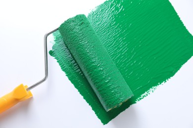 Photo of Smear of green paint and roller on white background, top view