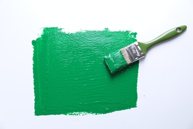 Photo of Smear of green paint and brush on white background, top view