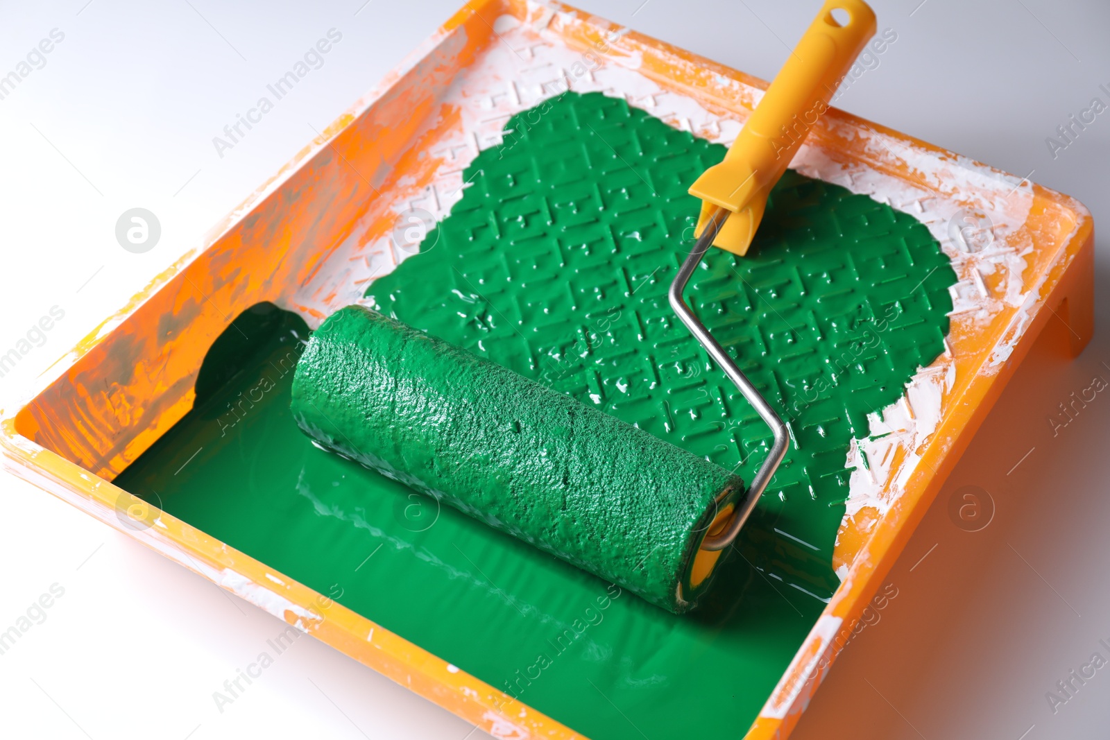 Photo of Tray with green paint and roller on white background, closeup