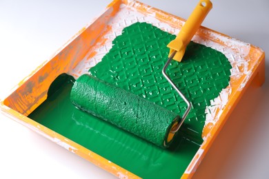 Photo of Tray with green paint and roller on white background, closeup