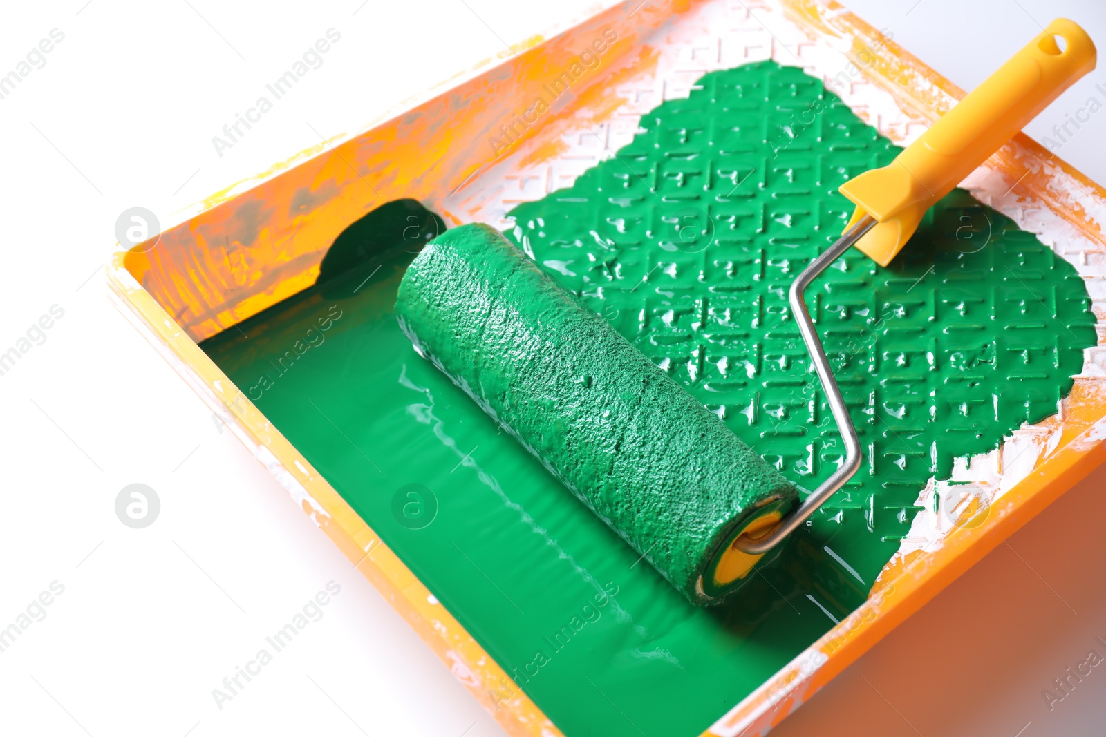 Photo of Tray with green paint and roller on white background, closeup