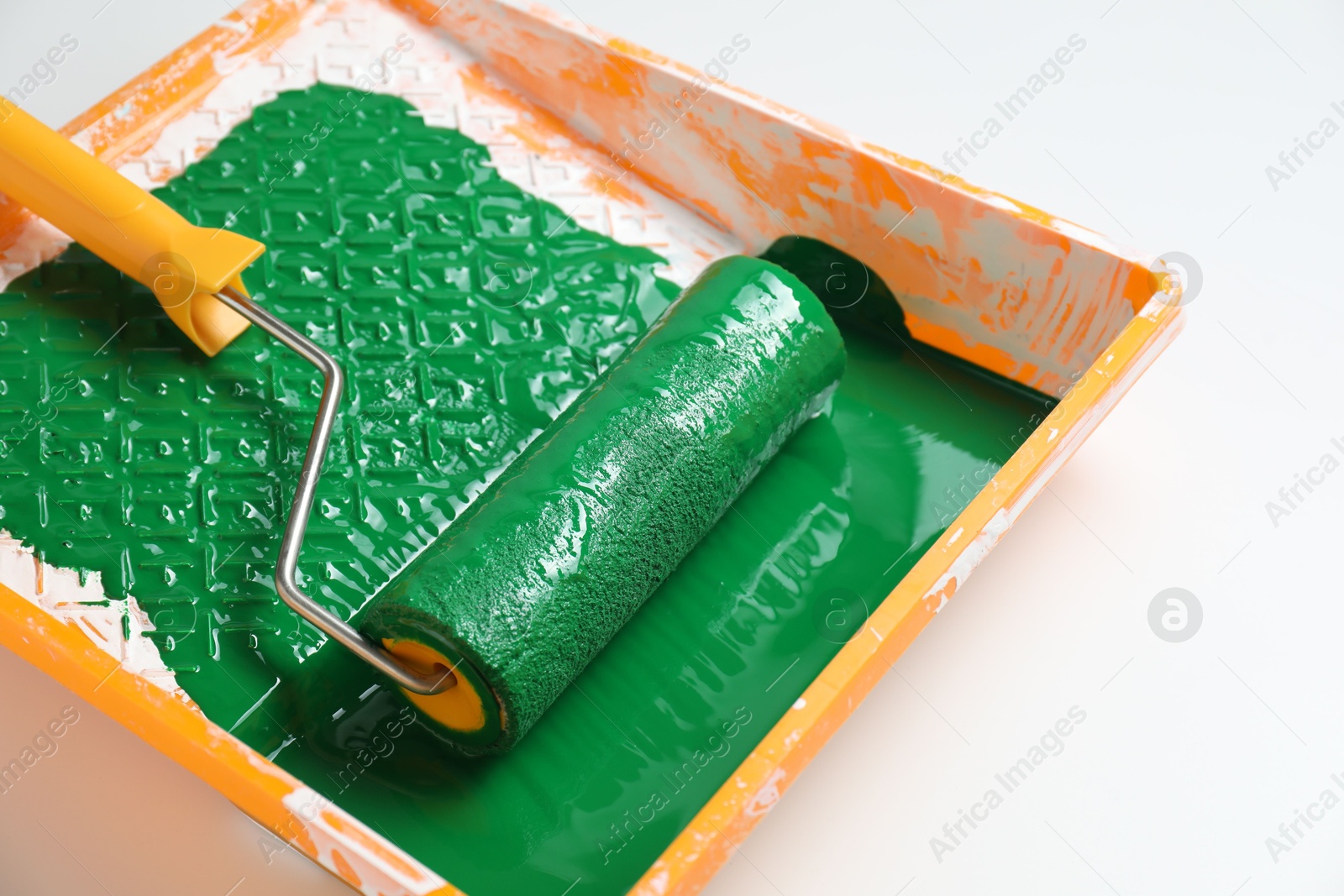 Photo of Tray with green paint and roller on white background, closeup