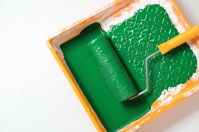 Photo of Tray with green paint and roller on white background, top view. Space for text