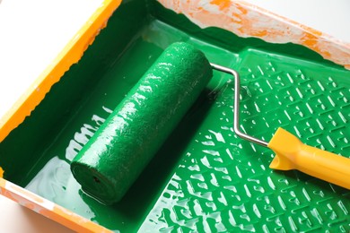 Tray with green paint and roller on white background, closeup