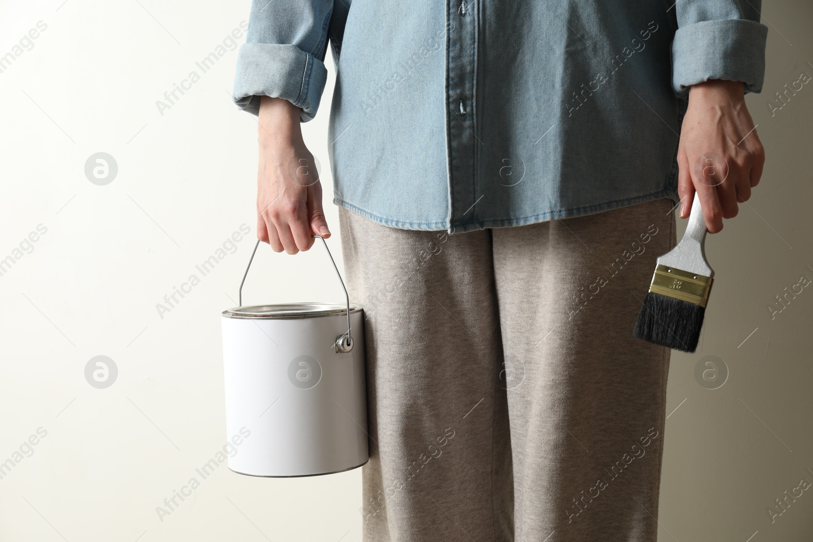 Photo of Woman holding bucket of paint and brush on white background, closeup