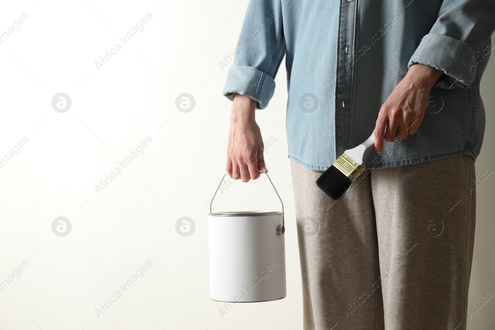 Photo of Woman holding bucket of paint and brush on white background, closeup. Space for text