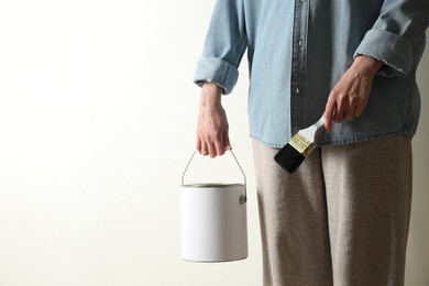 Woman holding bucket of paint and brush on white background, closeup. Space for text