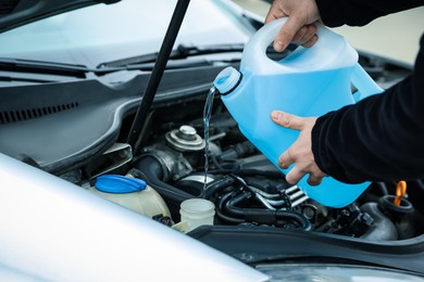 Photo of Man pouring windshield washer from plastic canister into car reservoir, closeup