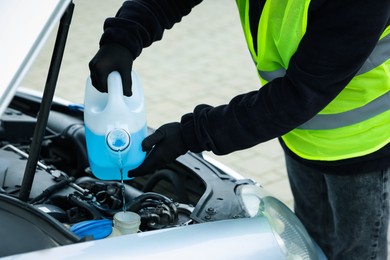 Photo of Man pouring windshield washer from plastic canister into car reservoir outdoors, closeup