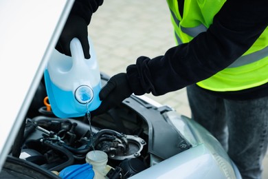 Photo of Man pouring windshield washer from plastic canister into car reservoir outdoors, closeup