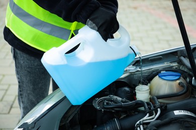 Man pouring windshield washer from plastic canister into car reservoir outdoors, closeup