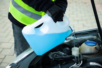 Photo of Man pouring windshield washer from plastic canister into car reservoir outdoors, closeup