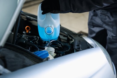 Photo of Man pouring windshield washer from plastic canister into car reservoir, closeup