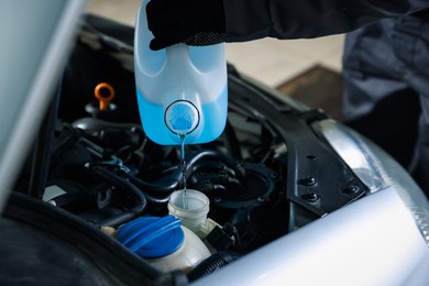 Photo of Man pouring windshield washer from plastic canister into car reservoir, closeup