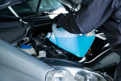 Photo of Man pouring windshield washer from plastic canister into car reservoir, closeup