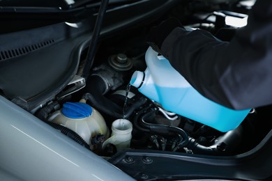 Photo of Man pouring windshield washer from plastic canister into car reservoir, closeup