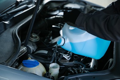 Man pouring windshield washer from plastic canister into car reservoir, closeup