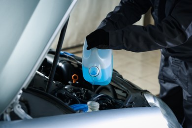 Photo of Man pouring windshield washer from plastic canister into car reservoir outdoors, closeup