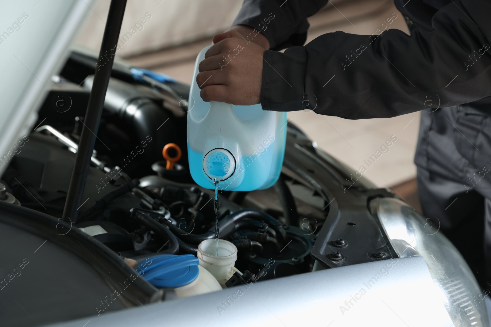 Photo of Man pouring windshield washer from plastic canister into car reservoir outdoors, closeup