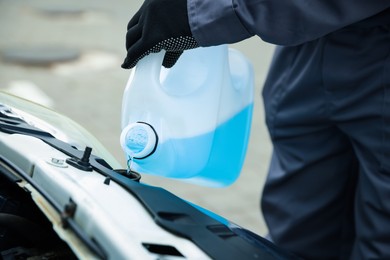 Photo of Man filling car radiator with antifreeze outdoors, closeup