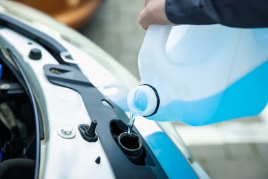 Photo of Man filling car radiator with antifreeze outdoors, closeup