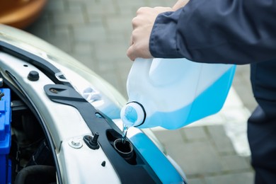 Photo of Man filling car radiator with antifreeze outdoors, closeup