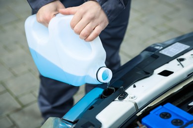 Photo of Man filling car radiator with antifreeze outdoors, closeup