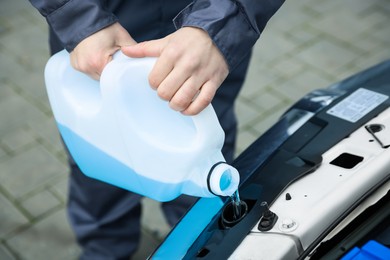 Photo of Man filling car radiator with antifreeze outdoors, closeup