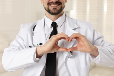 Smiling cardiologist making heart with hands indoors, closeup