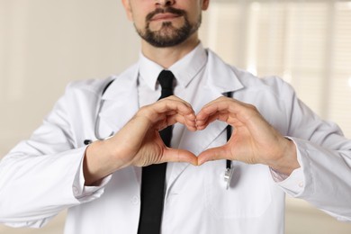 Photo of Cardiologist making heart with hands indoors, closeup