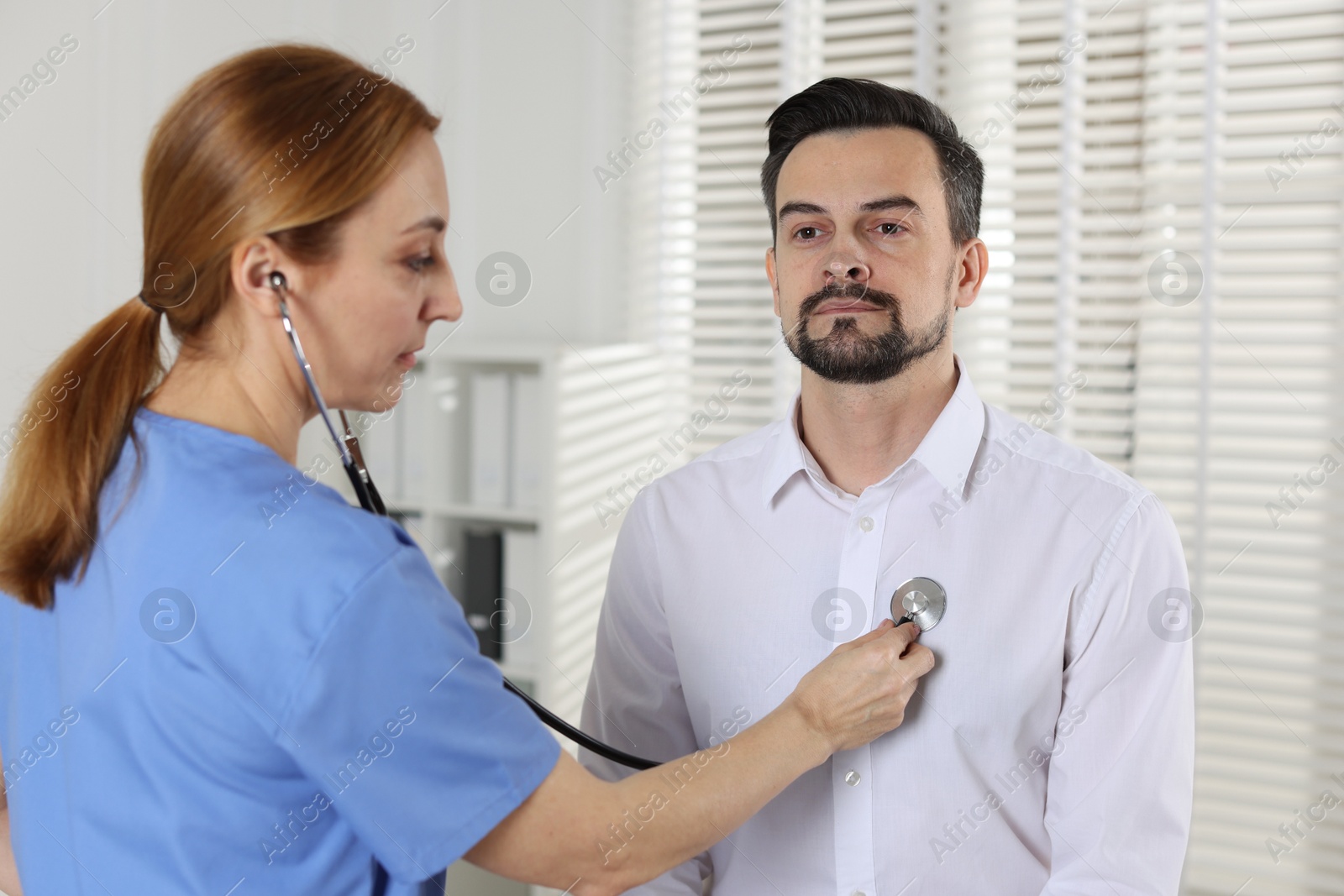 Photo of Cardiologist with stethoscope listening patient's heartbeat in hospital